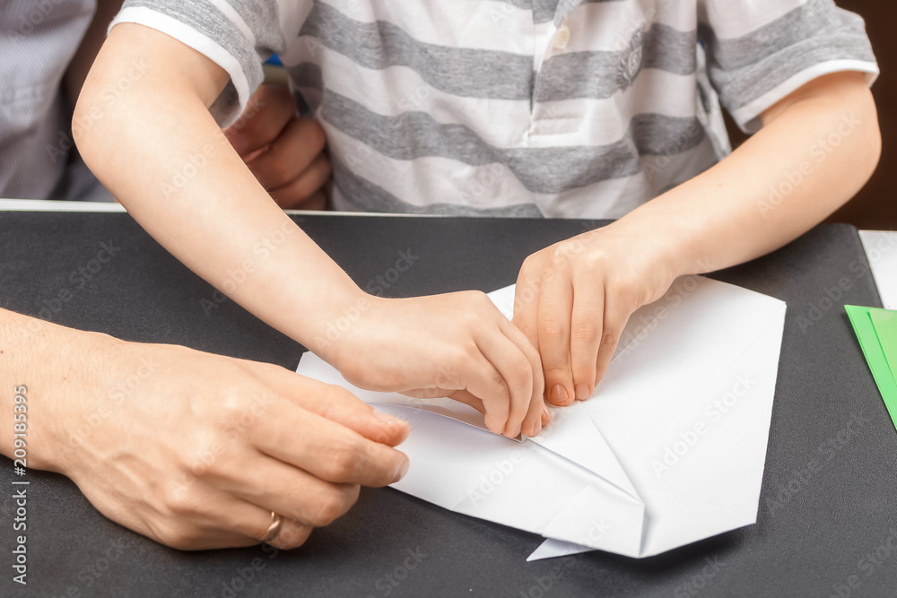 Process of folding a figure of origami from white paper together with a child and an adult. Close-up. The concept of joint family creativity, the transfer of experience from generation to generation