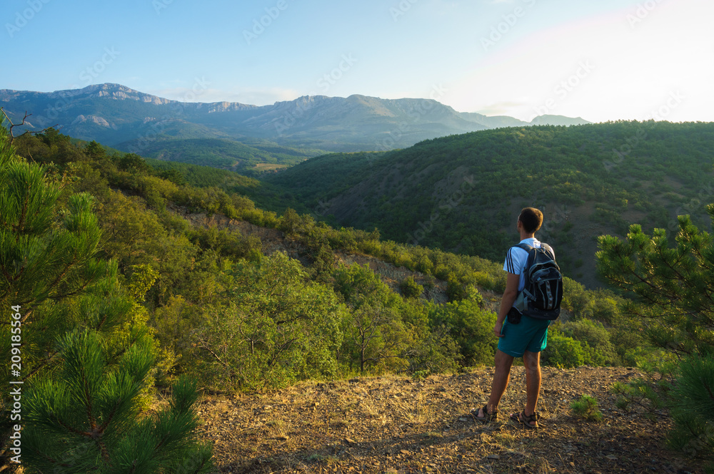 Fototapeta premium A young man stands on the edge of a rock and looks into the distance to the Crimean mountains. The Landscape Of Russia. Photo of a tourist.