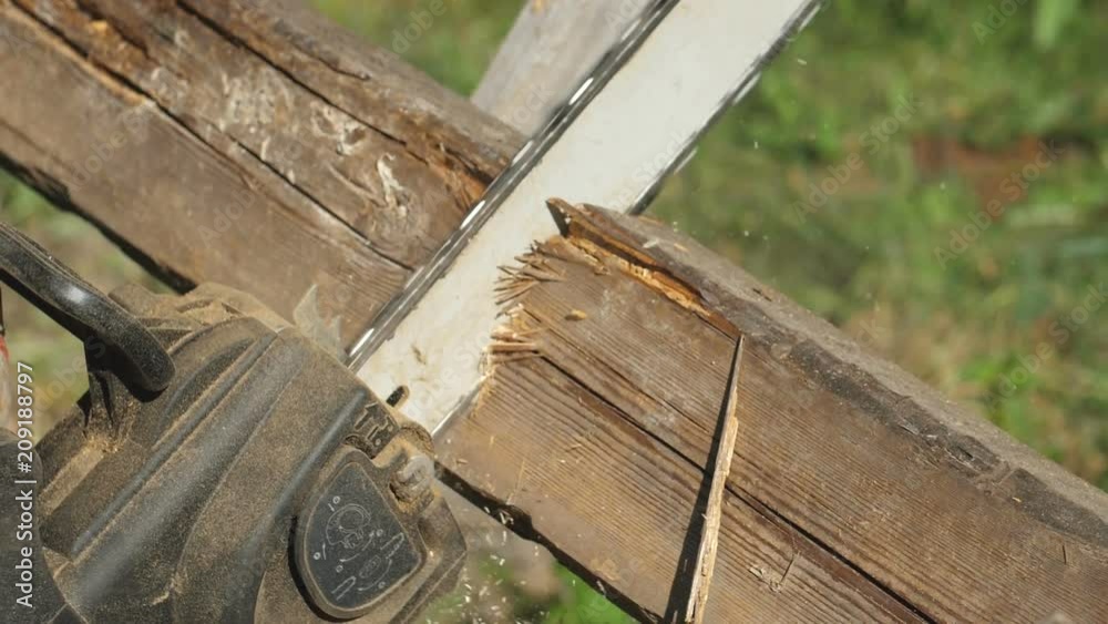 manual chainsaw cuts a wooden plank lying on a pole, sawed through a tree, slow cutting of a tree, macro shooting, background blurred manual chainsaw cuts a wooden plank lying on a pole, sawed through a tree, slow cutting of a tree, macro shooting, background blurred