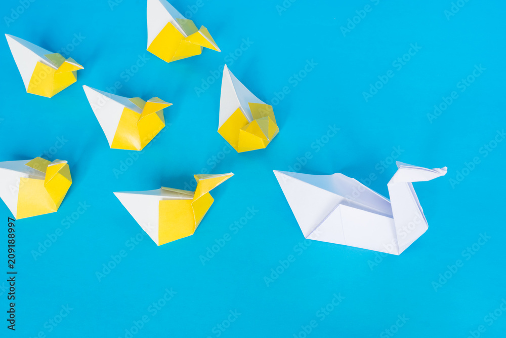 Unique and leadership concept, paper origami swan and ducks on the blue background. Unique and leadership concept, paper origami swan and ducks on the blue background.