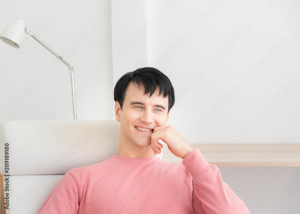 Portrait of a satisfied man relaxing with the arms in the head sitting on a chair at home with a warm light from a window. young man indoors with very handsome face in pink casual shirt Portrait of a satisfied man relaxing with the arms in the head sitting on a chair at home with a warm light from a window. young man indoors with very handsome face in pink casual shirt