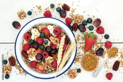 Healthy vegetarian breakfast food concept with fresh fruit, muesli, pollen grain, yoghurt & nuts on rustic wood table background with wheat sheaths. Super food high in omega 3, protein & antioxidants.