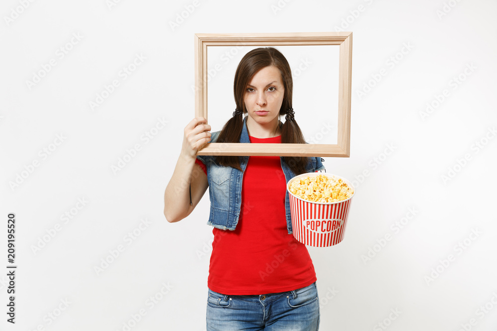 Portrait of young serious pretty brunette woman watching movie film, holding bucket of popcorn and picture frame, looking aside on copy space isolated on white background. Emotions in cinema concept. Portrait of young serious pretty brunette woman watching movie film, holding bucket of popcorn and picture frame, looking aside on copy space isolated on white background. Emotions in cinema concept.