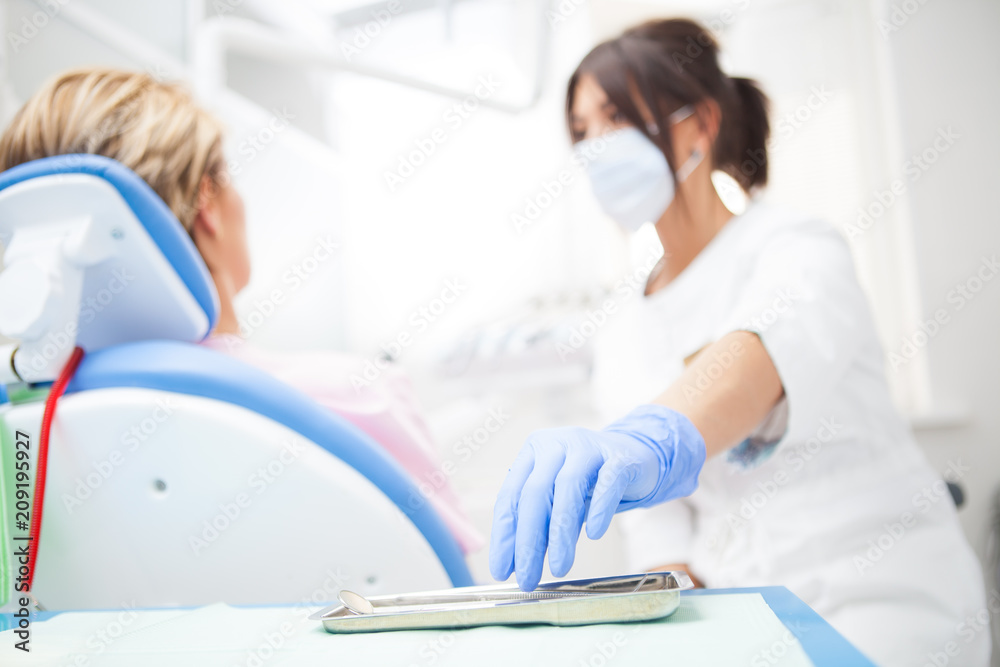 Obraz premium A close-up photo of a dentist's hand taking a sterile instrument from a metal tray. Focus on the doctor's hand