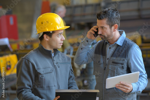 male supervisor talking on mobile phone with worker at industry photo