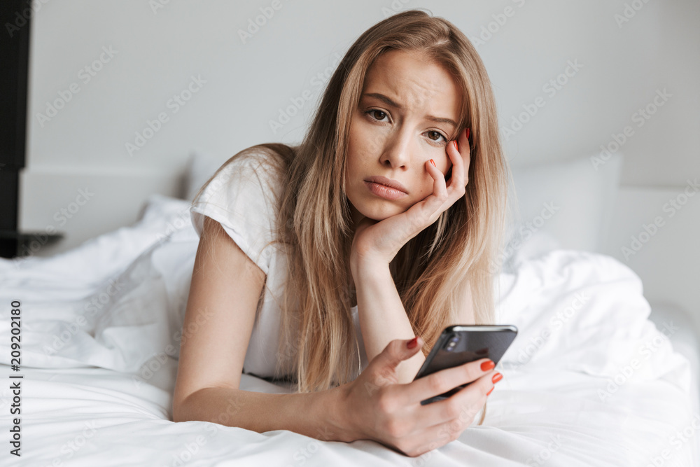 Sad woman lies on bed indoors looking camera. Sad woman lies on bed indoors looking camera.