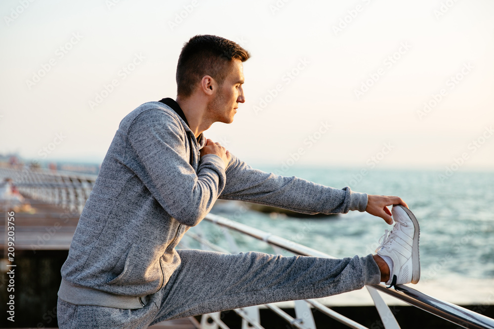Young attractive man in sportswear on workout , doing exercises for legs, on quay, outdoors. Young attractive man in sportswear on workout , doing exercises for legs, on quay, outdoors.