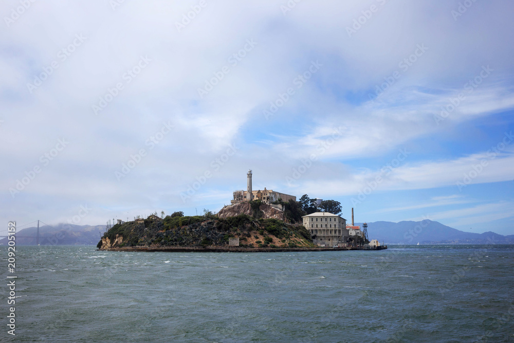 Alcatraz Island in the middle of San Francisco Bay, under blue sky and fog