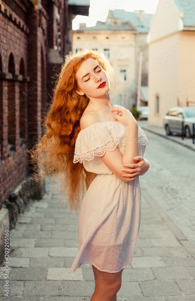 Tender ginger girl with long hair wearing white dress with naked shoulders