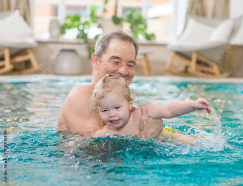Senior man teaches to swim his little granddaughter in the pool