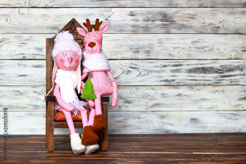 Doll-toy of a pink rabbit girl in a white hat with a green fir-tree and deer sitting on a chair. Love, romantic and friendship. Concept of joy and winter holidays photo