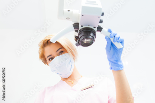 Professional dental endodontic binocular microscope in a treatment room A female doctor looks at the camera. Bottom view © Dmitry