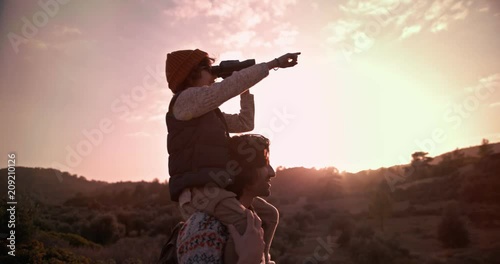 Boy on hiker father's shoulders using binoculars for bird watching photo