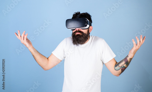 Man with hipster beard in idk posture isolated on blue background. Bearded software developer clueless about program bug in new VR equipment. Bearded man in virtual reality glasses testing new gadget photo