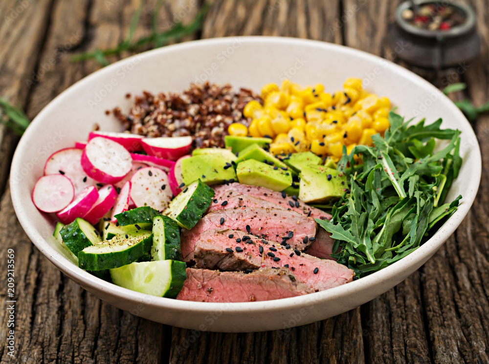 Healthy dinner. Buddha bowl lunch with grilled beef steak and quinoa, corn, avocado, cucumber and arugula on wooden background. Meat salad. Healthy dinner. Buddha bowl lunch with grilled beef steak and quinoa, corn, avocado, cucumber and arugula on wooden background. Meat salad.