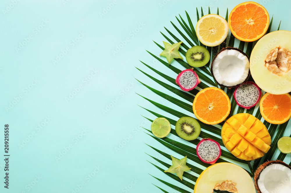 Fototapeta Egzotyczne owoce i tropikalne liście palmowe na pastelowym turkusowym tle - papaja, mango, ananas, banan, carambola, smok owoc, kiwi, cytryna, pomarańcza, melon, kokos, wapno. Widok z góry.