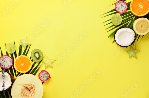 Fototapeta Naklejka Na Ścianę i Meble -  Exotic fruits and tropical palm leaves on pastel yellow background - papaya, mango, pineapple, banana, carambola, dragon fruit, kiwi, lemon, orange, melon, coconut, lime. Top view.