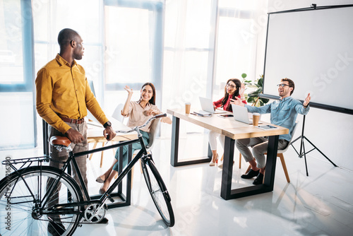 multicultural business people greeting african american colleague with bicycle in office