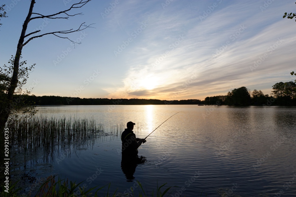 Silhouette of fisherman standing in the lake and catching the fish during sunrise
