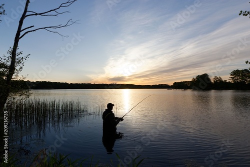 Silhouette of fisherman standing in the lake and catching the fish during sunrise 