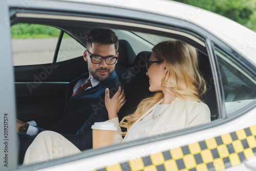 smiling young woman holding paper cup and flirting with handsome man sitting in taxi © LIGHTFIELD STUDIOS