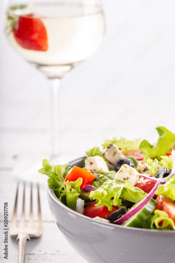 Fresh greek salad served in bowl with glass of white wine. Fresh greek salad served in bowl with glass of white wine.