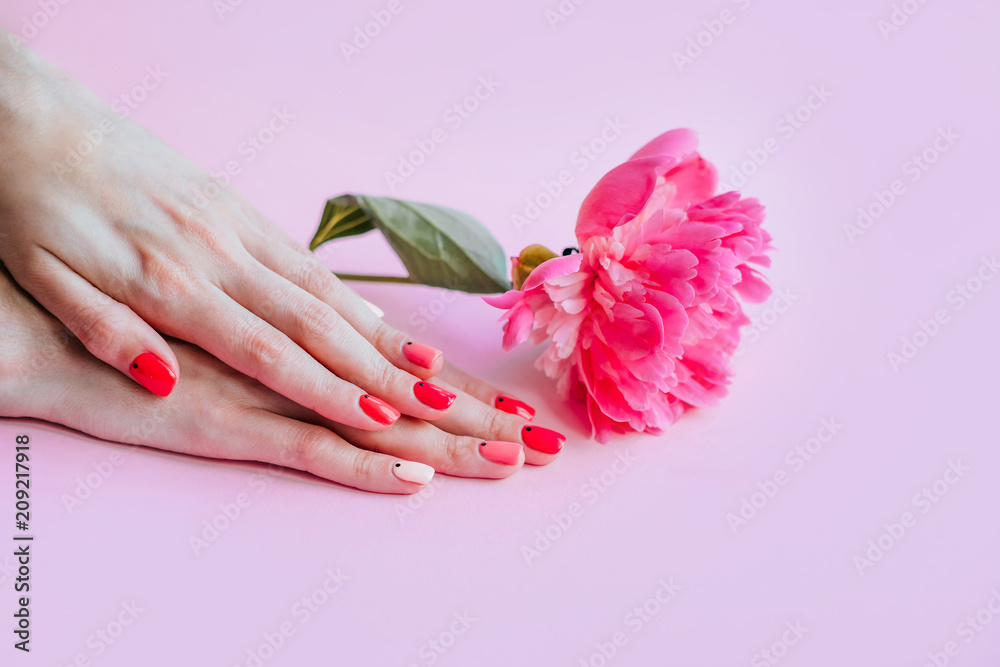Creative bright trendy summer manicure with nails of different color. Female hands with art nail design on pink background and fuchsia peony flower.