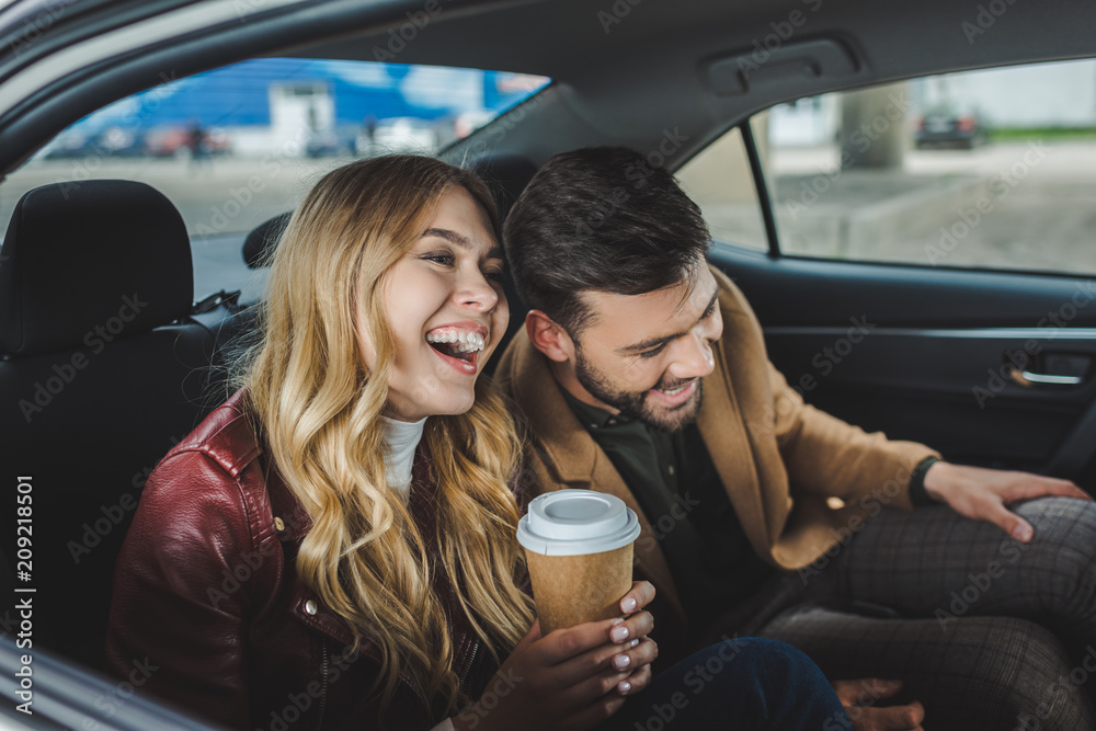 happy young couple laughing while sitting together in taxi - obrazy, fototapety, plakaty 