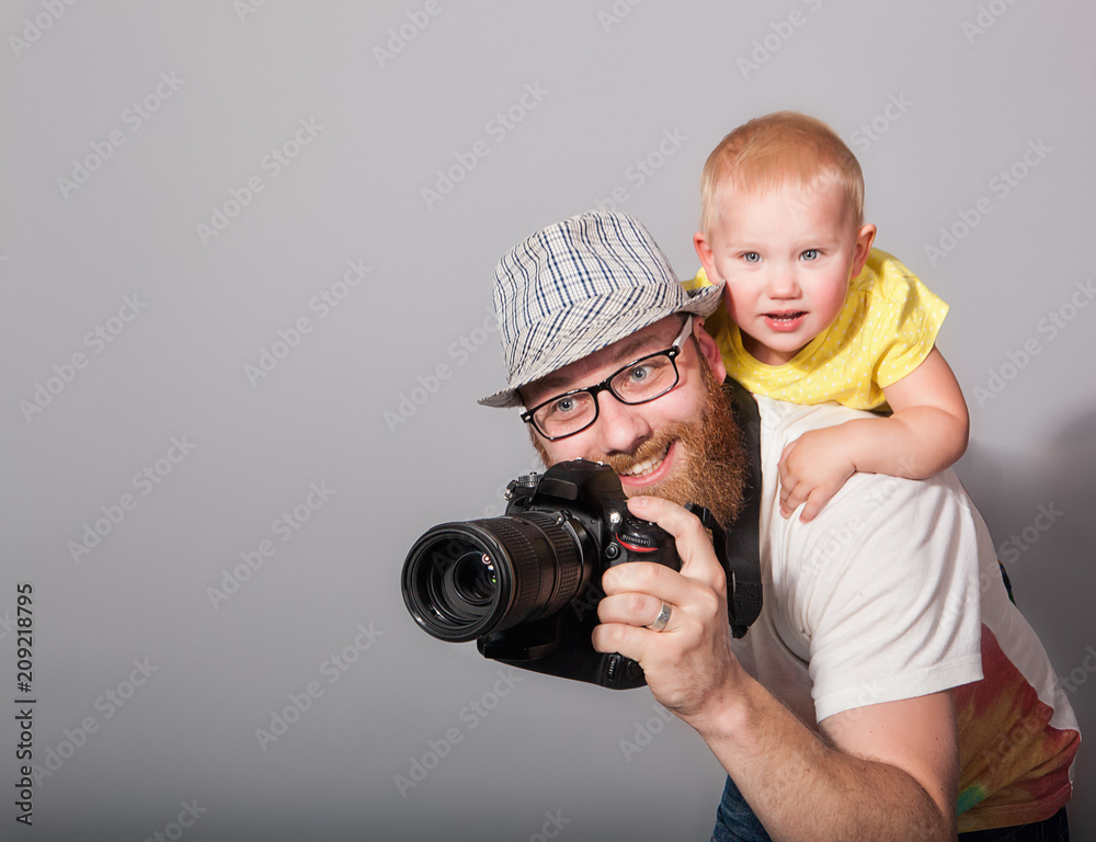 A photographer with a child in his arms takes an enthusiastic photograph against a gray background in the studio. The concept of 
