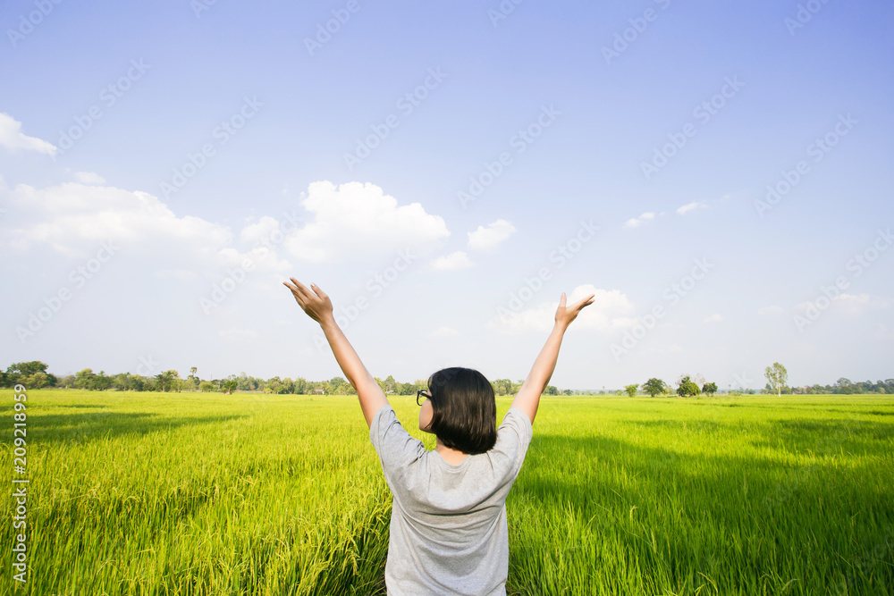 Beautiful woman standing with raised arms on rice field green grass and blue sky. Rice green farmer's farm. Scenic view of the landscape paddy field at thailand Beautiful woman standing with raised arms on rice field green grass and blue sky. Rice green farmer's farm. Scenic view of the landscape paddy field at thailand