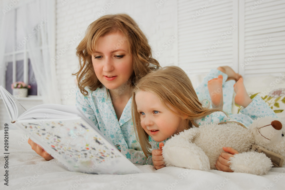 Family reading bedtime. Pretty young mother reading a book to her daughter. Mother reads a fairy tale to her daughter. A fairy tale for the night. Mom teaches my daughter to read Family reading bedtime. Pretty young mother reading a book to her daughter. Mother reads a fairy tale to her daughter. A fairy tale for the night. Mom teaches my daughter to read