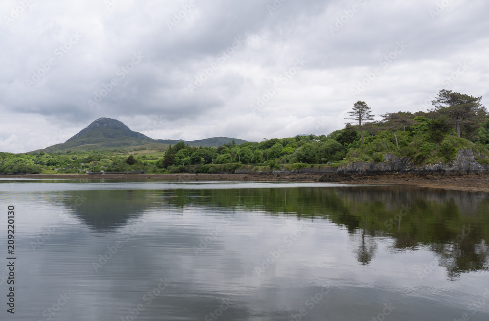 Beautiful beach, with mountains in the background and cloudy skies, with forest along the coast. Taken in Letterfrack along the Wild Atlantic Way, Ireland in summer.