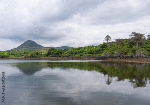 Beautiful beach, with mountains in the background and cloudy skies, with forest along the coast. Taken in Letterfrack along the Wild Atlantic Way, Ireland in summer.