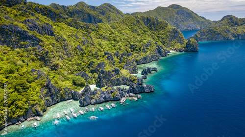 Aerial drone view of tourist boats over a tropical coral reef and small sandy because in the Bacuit Archipelago