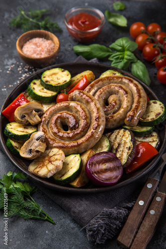 grilled spiral sausages and vegetables on dark plate