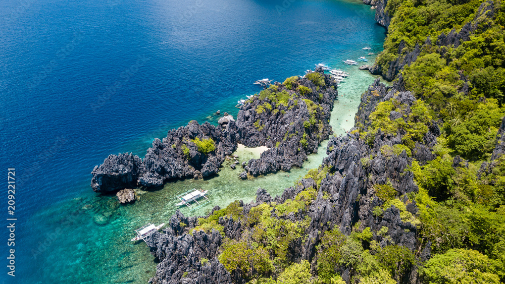 Aerial drone view of traditional banca boats next to a coral reef and beautiful, shallow tropical lagoon