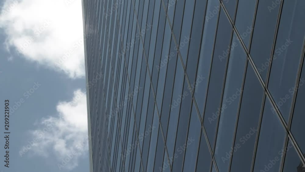 Glass facade of skyscraper building against gray blue sky and running clouds. Concept of business, global finance, economy and communication.