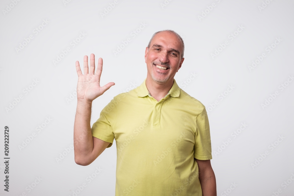 Friendly-looking attractive european man waives hand in hello gesture while smiling cheerfully. Host is glad to welcome his guests or friends Friendly-looking attractive european man waives hand in hello gesture while smiling cheerfully. Host is glad to welcome his guests or friends