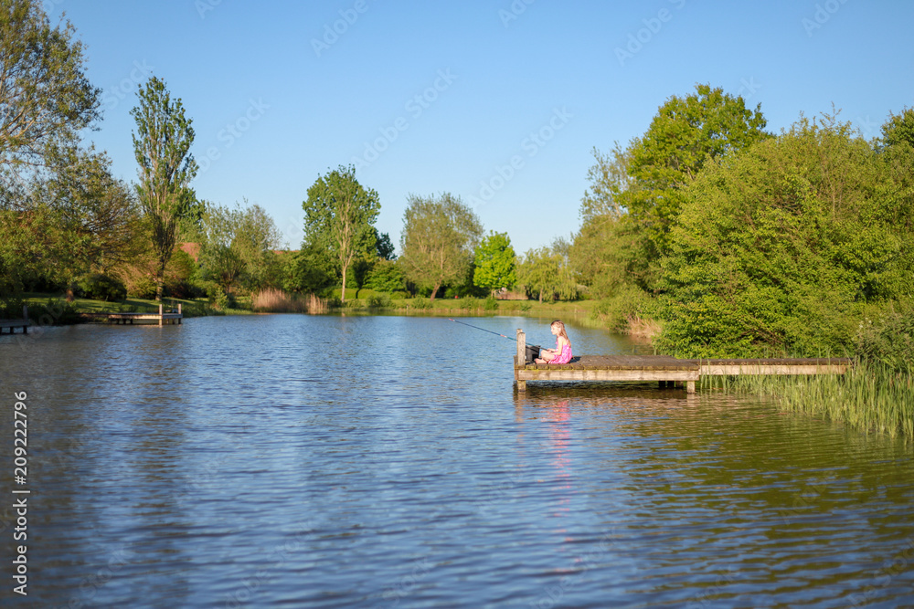 Ein Schulmädchen sitzt auf dem Steg an einem See und angelt