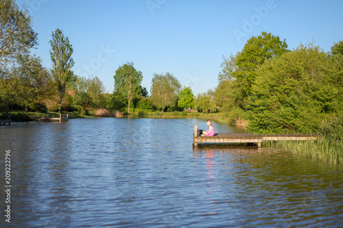 Ein Schulmädchen sitzt auf dem Steg an einem See und angelt