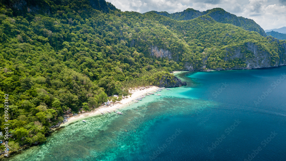 Aerial drone view of a spectacular tropical beach surrounded by dense jungle and jagged cliffs (Papaya Beach, Palawan)