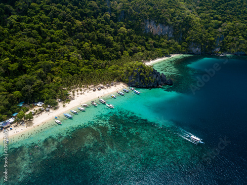 Aerial drone view of traditional Banca boats and coral reef surrounding a scenic tropical sandy beach (7 Commando Beach, El Nido)