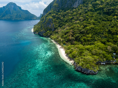 Aerial drone view of a spectacular tropical beach surrounded by dense jungle and jagged cliffs (Papaya Beach, Palawan)