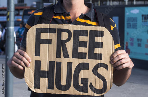 Man holding a cardboard sign with free hugs written on it