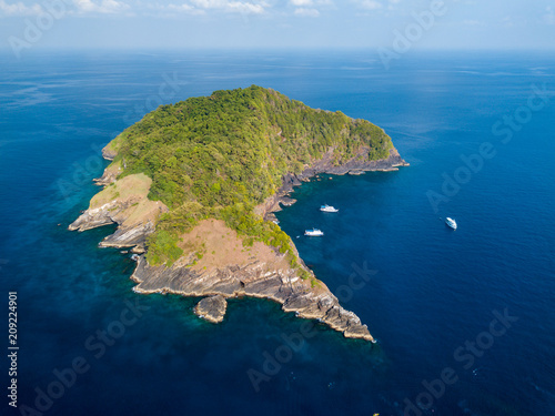 Aerial drone view of a remote tropical island surrounded by coral reef and several diving boats