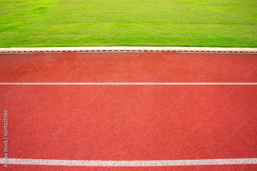 Fototapeta premium White lines of stadium and texture of running racetrack red rubber racetracks in outdoor stadium are 8 track and green grass field,empty athletics stadium with track,football field, soccer field.