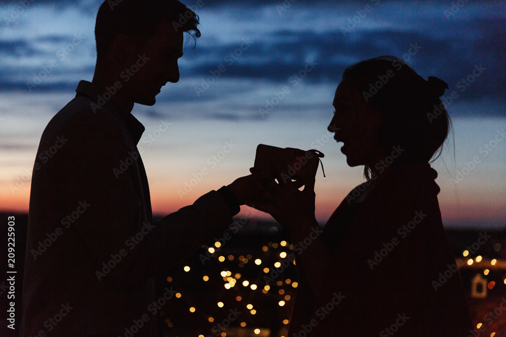 Man gives a present to a woman standing on the rooftop in the night