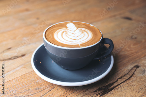 Closeup image of a blue cup of hot latte coffee with latte art on vintage wooden table in cafe