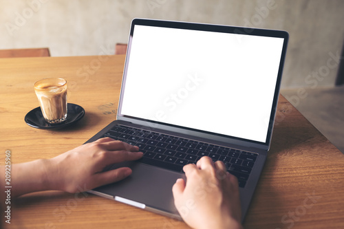 Mockup image of a woman using laptop with blank white desktop screen with coffee cup on wooden table