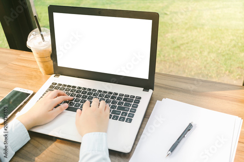 Close-up of business female working with laptop with blank white screen make a note document and smartphone in coffee shop like the background.